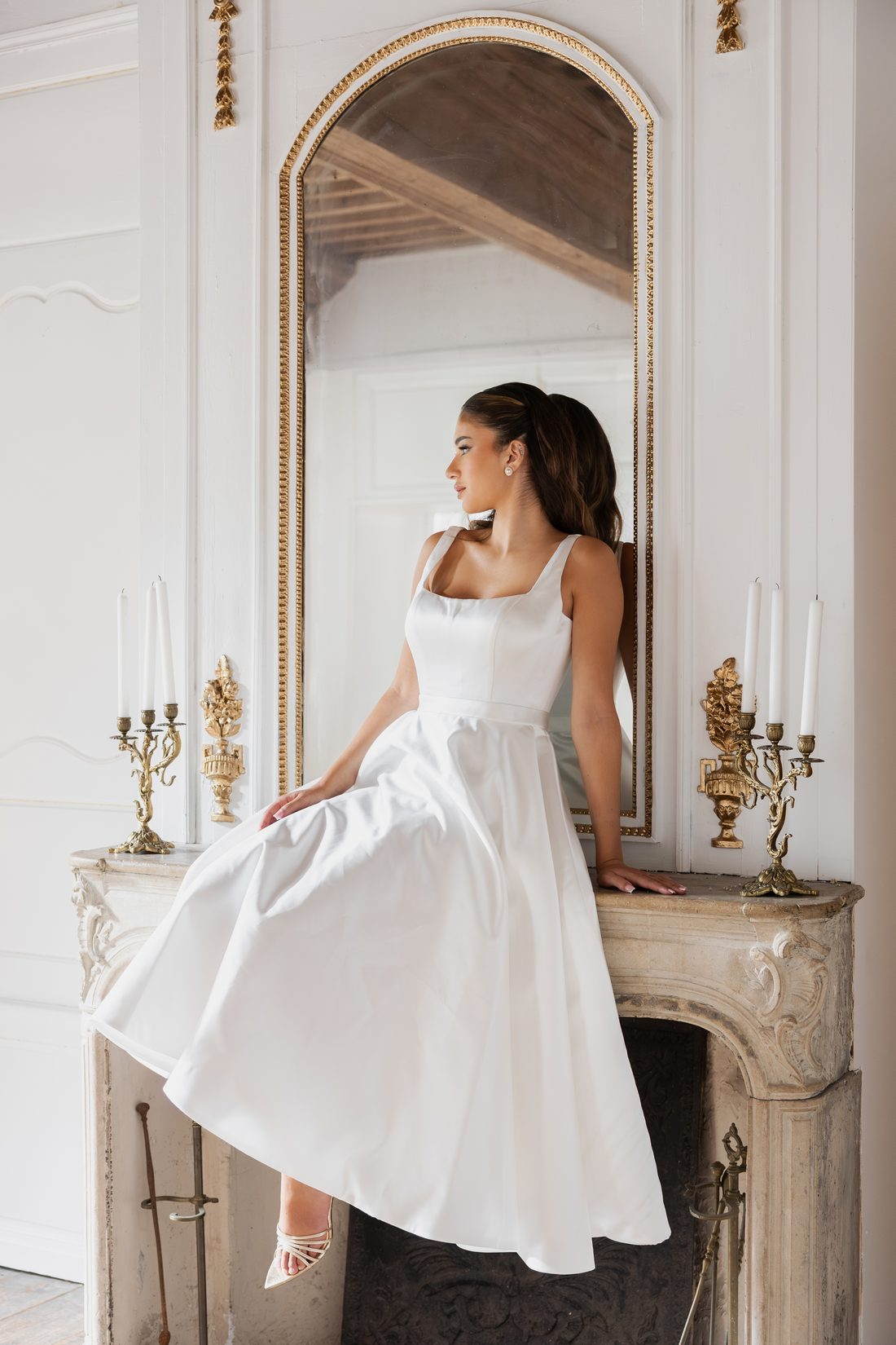 Robe de mariée en satin à bretelles larges, assise devant un miroir doré